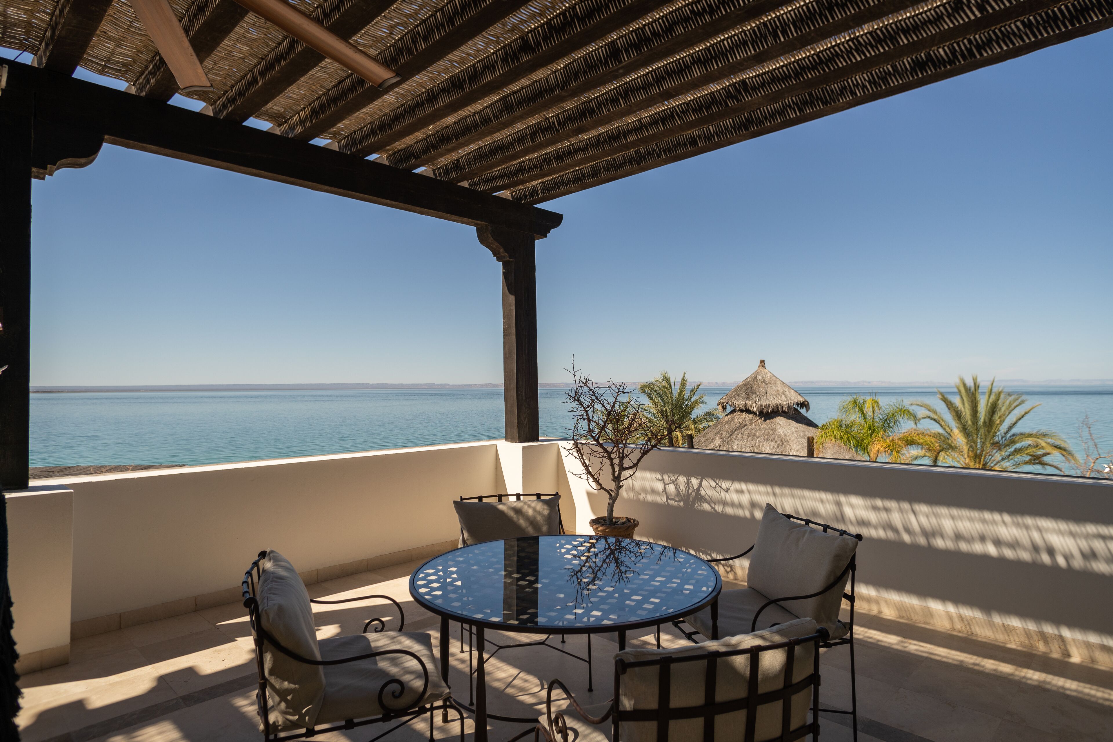 Eine Terrasse mit rundem Tisch und Stühlen, mit Blick aufs Meer.