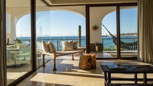 A spacious balcony with a view of the sea, furnished with a sofa, a wooden stool, and a table.