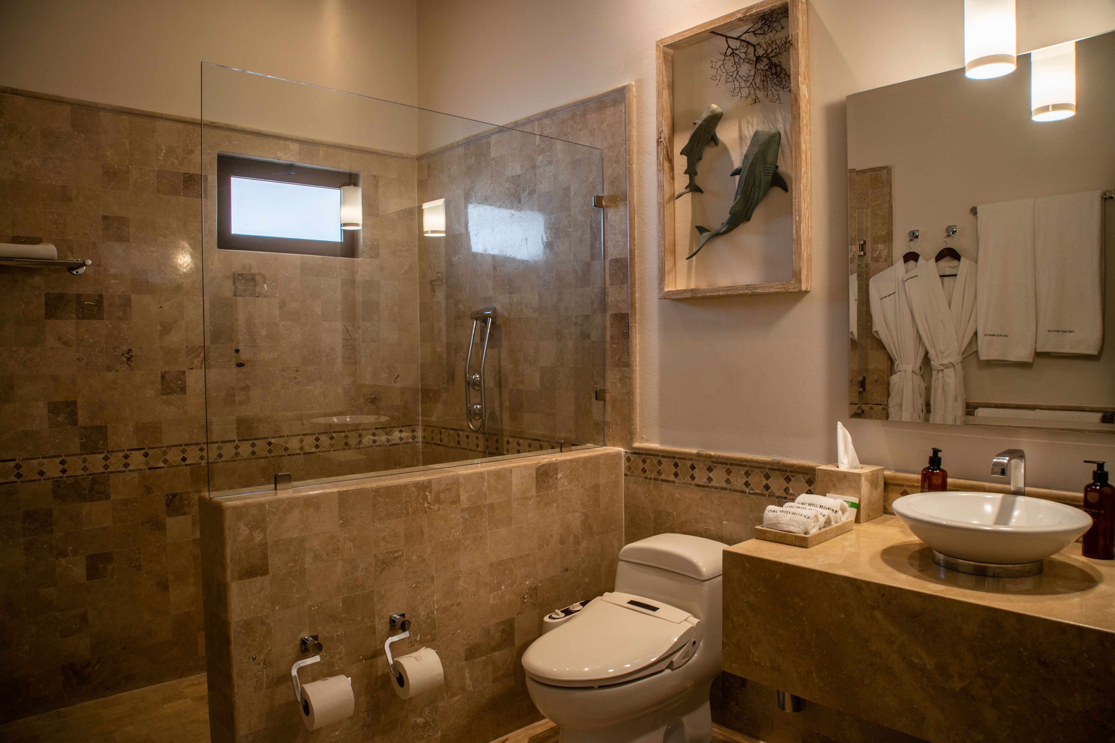 Un baño moderno con ducha de vidrio, inodoro, lavabo y espejo con un cuadro enmarcado.