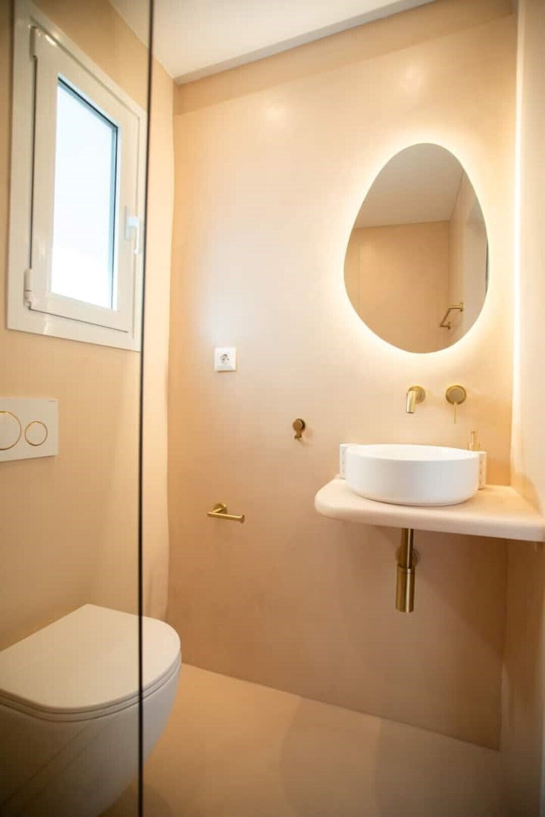 A modern bathroom with a toilet, a round mirror, and a white sink.