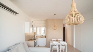 Een moderne woonkamer met een witte bank, een eettafel met stoelen, en een keuken op de achtergrond.