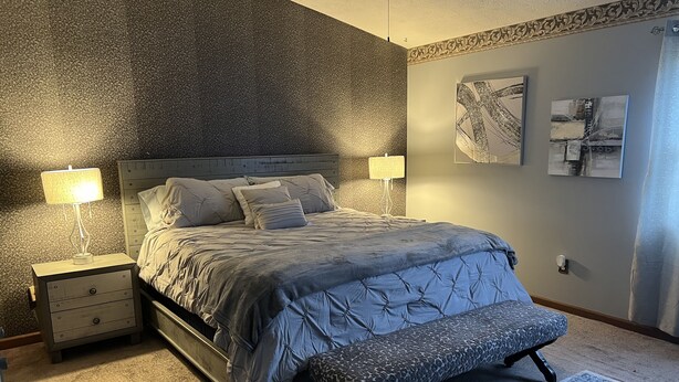 A bedroom with a bed, bedside tables, a bench, and wall art.