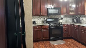 A kitchen with dark wooden cabinets, a black refrigerator, a microwave, a stove, and a coffee maker.