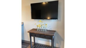 Un televisor de pantalla plana montado en la pared sobre un mueble consola de madera con un florero de flores amarillas.