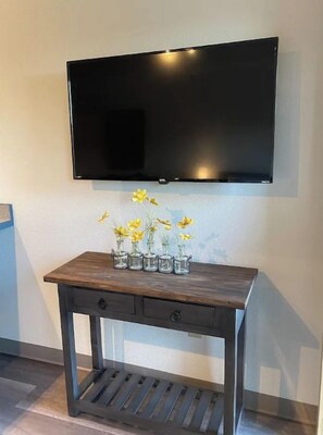 Een flatscreen televisie bevestigd aan de muur boven een houten console met een vaas gele bloemen.