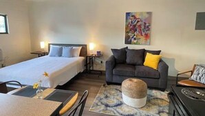 Una habitación de hotel con una cama grande, un sofá, un pequeño taburete, una mesa de comedor y un cuadro en la pared.