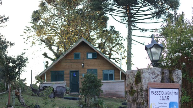 Een houten huis met een schuin dak, een pad van stenen en een bordje met de tekst 'Passeio Ingaí, 110 Luar'.
