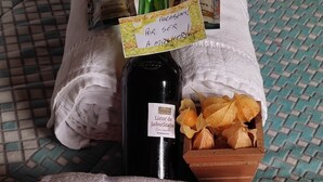Een net opgemaakt bed met een bedsprei met patroon, een fles drank, een klein houten doosje met chocolade en een decoratieve bloem.