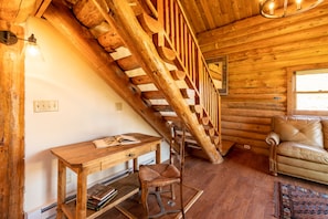 A wooden interior with a staircase, a leather sofa, a wooden table, and a chair. - East Glacier Cabin w/ Stunning Views of the Rockies! 30 min from 2 GNP entrances (Browning)