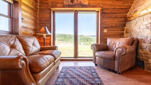 Interno di una baita in legno con divani in pelle, un tappeto decorato e un'ampia finestra che si affaccia sull'esterno.