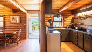 Una baita di legno con interni in legno, una sala da pranzo con sedie, una cucina con lavello e pensili, e vista sull'esterno.