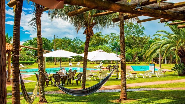 A poolside area with a hammock, lounge chairs, and umbrellas. - Botânico Hotel Fazenda e SPA (Aracatuba)