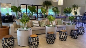A spacious lobby with a sofa set, round tables, and potted plants. - Botânico Hotel Fazenda e SPA (Aracatuba)