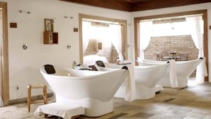 A spa room with three white tubs, wooden beams on the ceiling, and a brick wall visible through the windows. - Botânico Hotel Fazenda e SPA (Aracatuba)