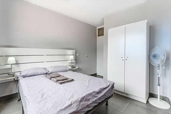 A modern bedroom with a bed, bedside lamps, a wardrobe, and a standing fan.