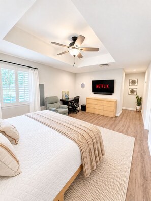 A modern bedroom with a bed, a desk, a chair, a TV, and a ceiling fan. - Relocation? Insurance Claim? Rehab? Best LOCATION in Flower Mound (Flower Mound)
