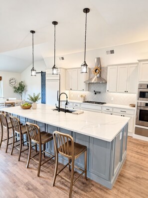 A modern kitchen with a large island, bar stools, stainless steel appliances, and pendant lighting.