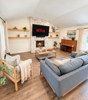 A living room with a fireplace, a television mounted on a brick wall, a piano, and a sofa. - Relocation? Insurance Claim? Rehab? Best LOCATION in Flower Mound (Flower Mound)