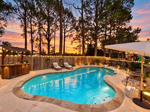 A backyard with a swimming pool, lounge chairs, and a wooden fence.