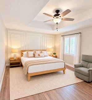 A bedroom with a bed, a ceiling fan, bedside lamps, a window with curtains, and a green armchair. - Relocation? Insurance Claim? Rehab? Best LOCATION in Flower Mound (Flower Mound)