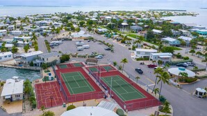 Ilmakuva rannikkoalueen asuinalueesta, jossa on useita tenniskenttää, vierasvenesatama ja taloja, joista on näkymät merelle.