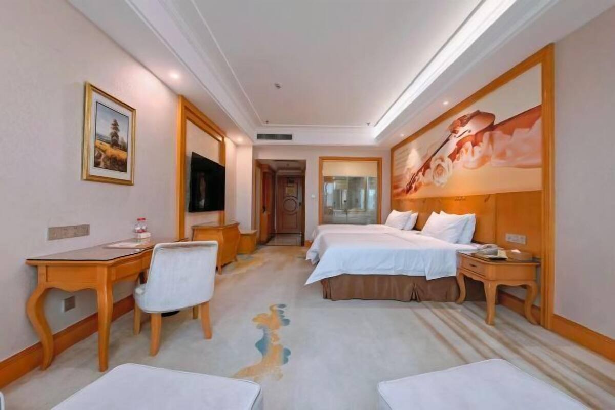 A hotel room with two beds, a desk, a chair, a television, and a painting on the wall.