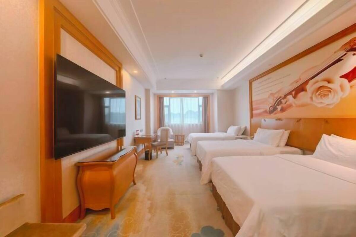 A hotel room with a TV, two beds, a desk, and a chair.