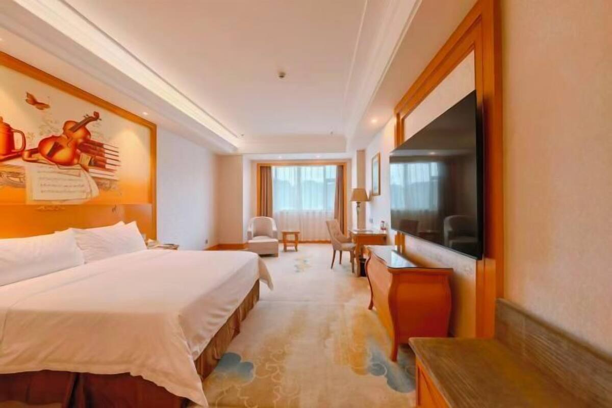 A hotel room with a bed, a desk, a chair, a TV, and a window.