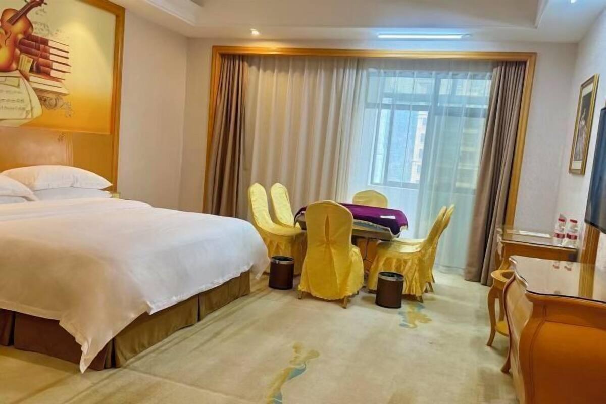 A hotel room with a bed, a desk with a chair, a table, and a window with curtains.