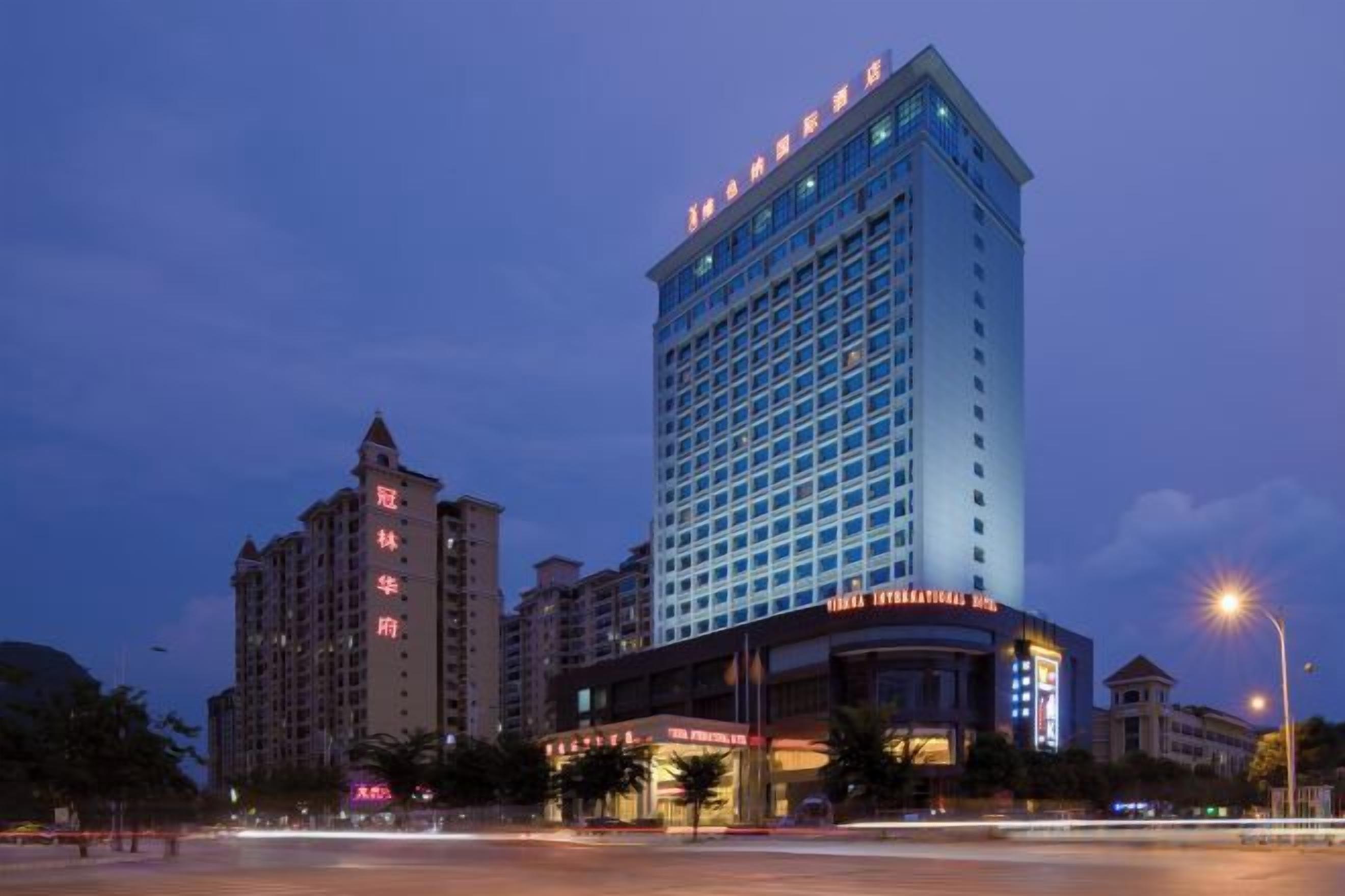 Un hotel de varios pisos con una ubicación destacada en una esquina, que cuenta con un letrero grande y ventanas iluminadas.