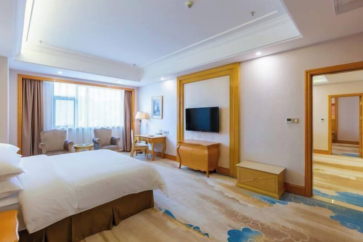 A hotel room with a large bed, a TV, a desk, and a chair.