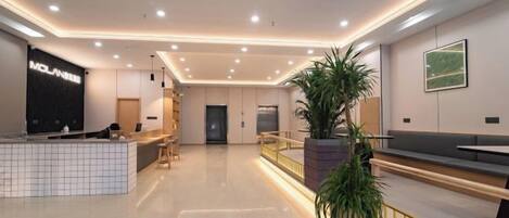 A modern hotel lobby with a reception desk, seating area, and a large potted plant.