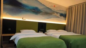 Une chambre d’hôtel avec deux lits, une literie verte, une grande fresque abstraite sur le mur et une table de chevet avec une lampe.