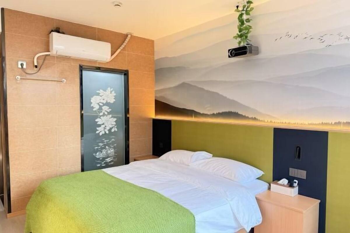 A hotel room with a bed, a nightstand, a wall-mounted air conditioner, and a decorative wall mural.