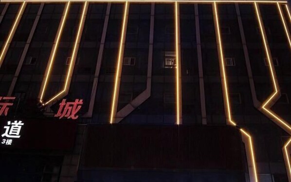 Fachada de edificio con líneas verticales iluminadas y señalización que indica una ubicación.