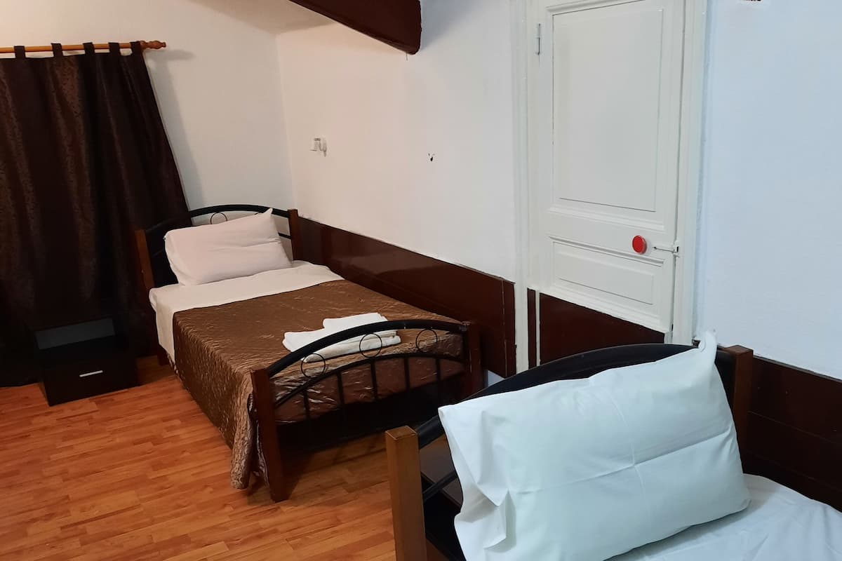 A room with two beds, wooden flooring, a white door with a red handle, and a curtain on the left.