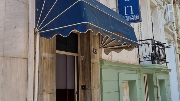 Fachada de hotel con toldo azul, un letrero que dice "HOTEL FERON" y una puerta verde.