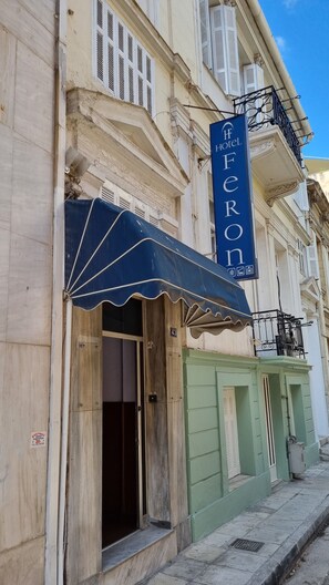 A hotel facade with a blue awning, a sign reading "HOTEL FERON," and a green door. - Hotel Feron (Athens)