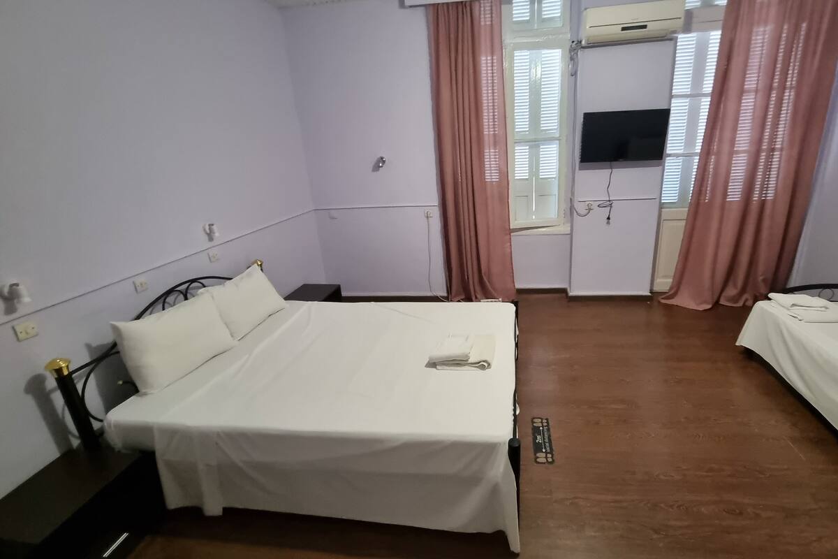 A small, clean room with a single bed, a bedside table, a desk, and a TV.