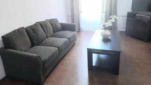 Una sala de estar con un sofá gris, una mesa de centro negra y un mueble para la televisión.