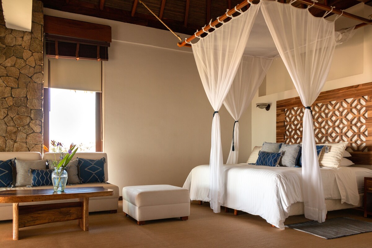 A bedroom with a canopy bed, a sofa, a coffee table, and a stone wall.