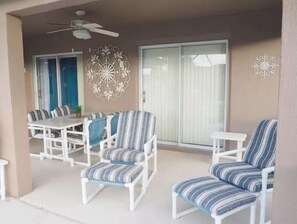 Ein Außenbereich mit Terrasse, weißen Möbeln, darunter ein Tisch und Stühle, sowie einem Deckenventilator.