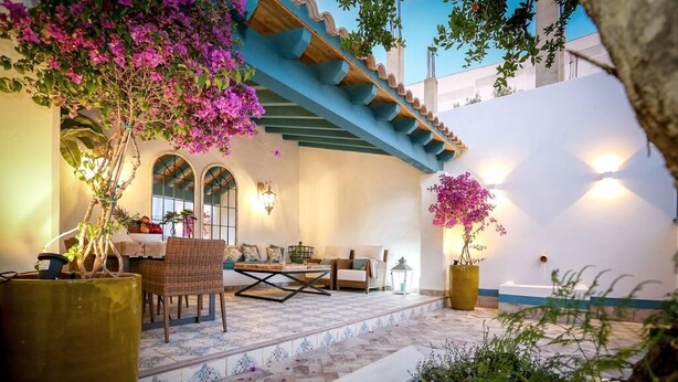 Une terrasse avec des sièges d’extérieur, des plantes en pot et un mur blanc orné d’une bordure bleue.