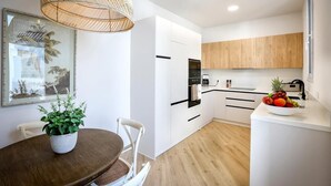 Une cuisine moderne avec des meubles blancs, un plan de travail en bois et un coin repas comprenant une table ronde et des chaises.