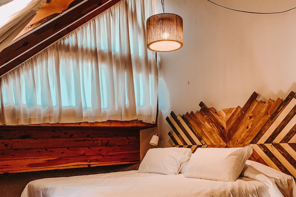 A cozy bedroom with a wooden headboard, a bed with white linens, and a hanging light fixture.