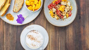 Une table en bois dressée pour le petit-déjeuner, avec des toasts, des fruits, du granola et une tasse de café.