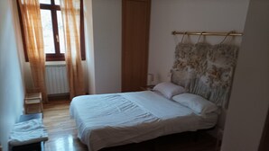 A bedroom with a bed, a nightstand, a chair, and a window with curtains. - The Corner of Azarrulla (Azarrulla)