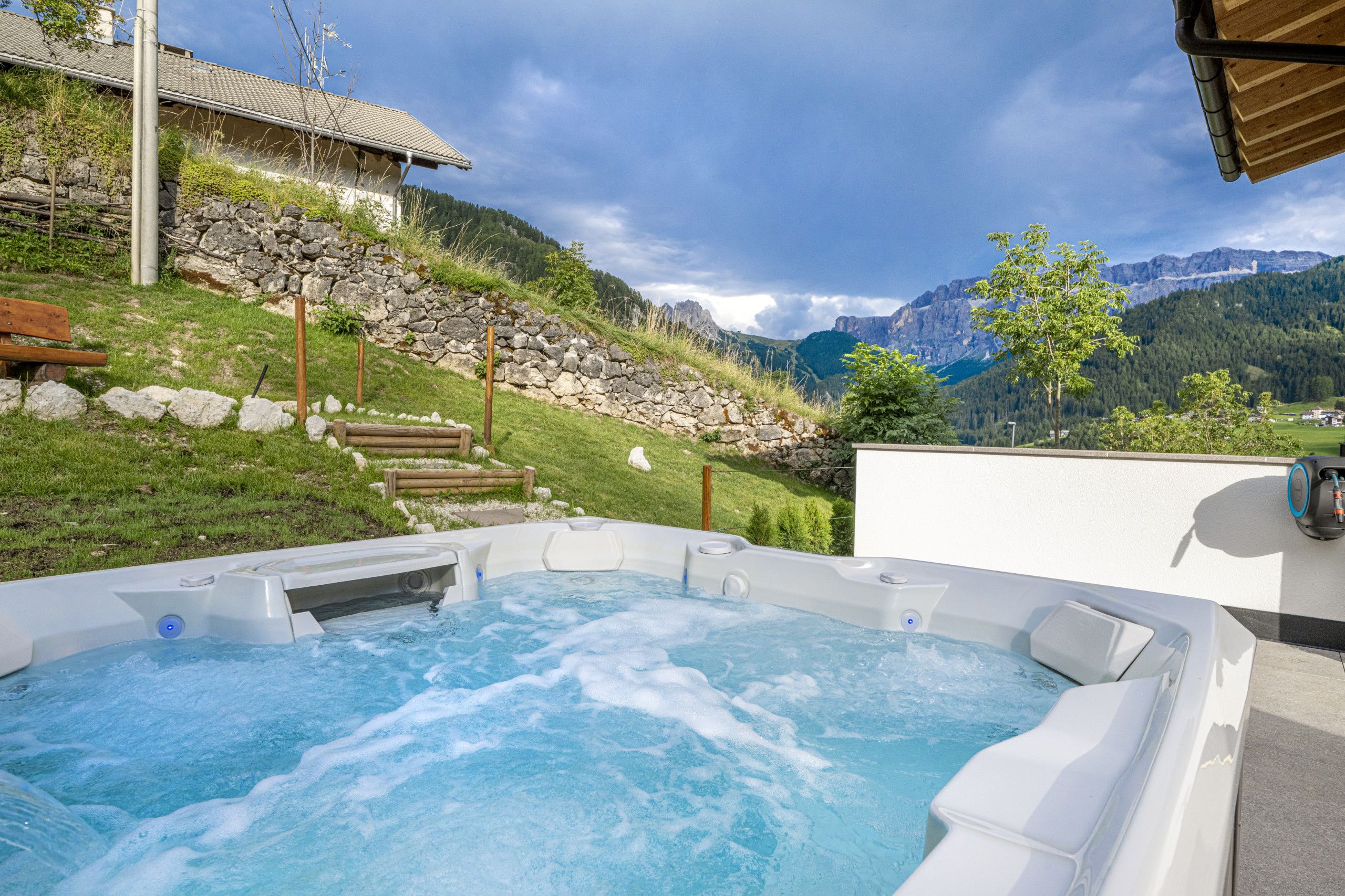 Un bain à remous avec vue sur les montagnes, un mur en pierre et un banc en bois.