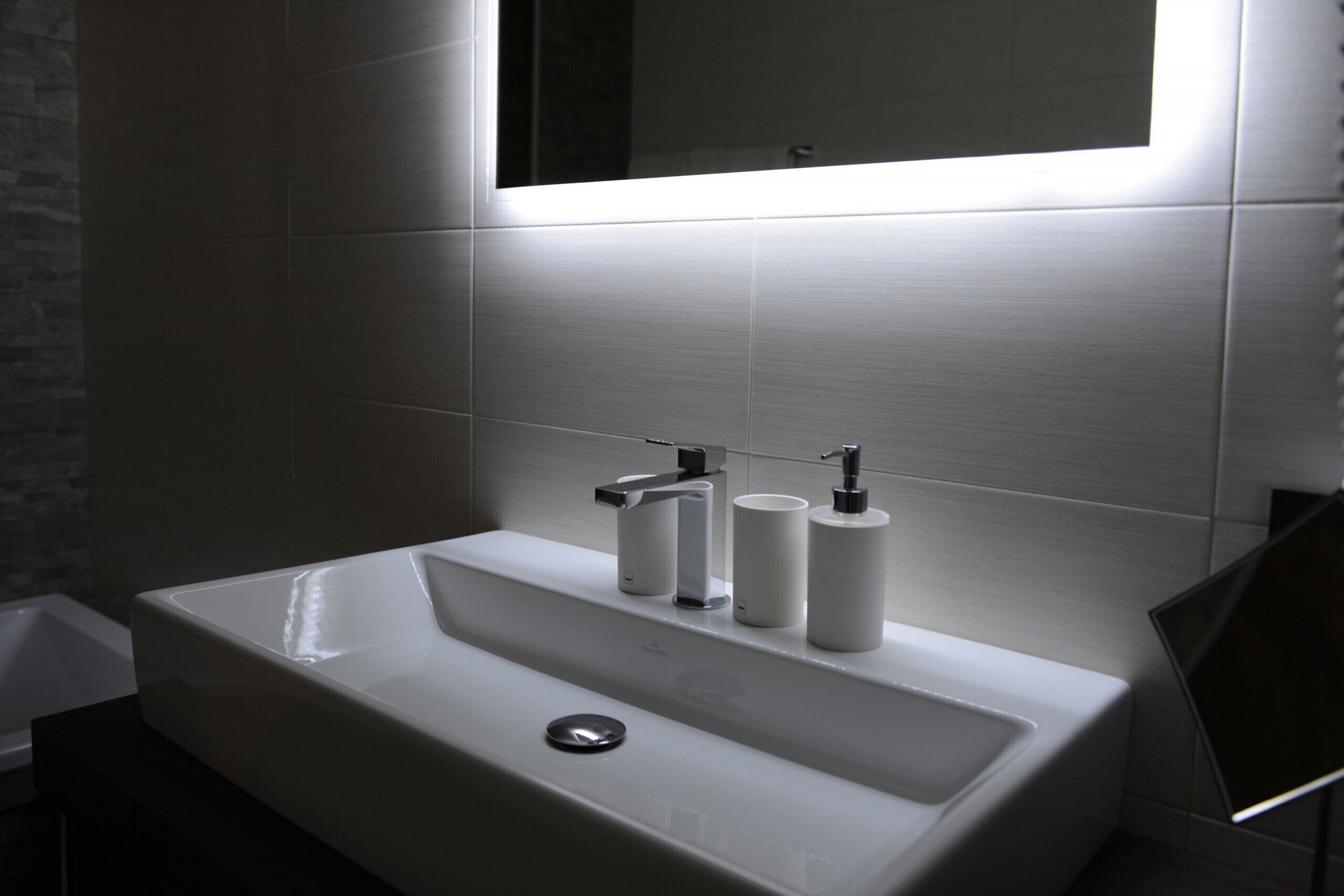 Un bagno moderno con un lavandino bianco, due rubinetti e uno specchio sopra.