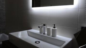 Un bagno moderno con un lavandino bianco, due rubinetti e uno specchio sopra.